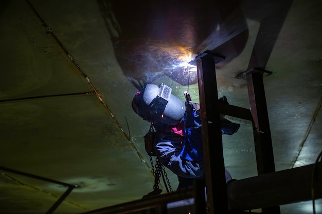 A soldagem do arco de metal do trabalhador masculino faz parte da construção do gasoduto do bocal do tanque de máquinas, óleo de petróleo e tanque de armazenamento de gás dentro de espaços confinados.