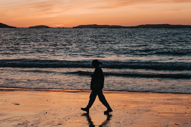 A sombra de uma mulher caminhando em frente a uma praia durante o pôr do sol