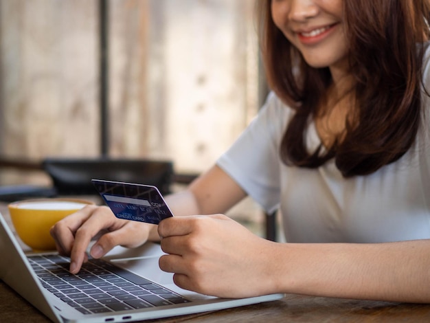 A sorridente jovem asiática gosta de fazer compras on-line por meio de um computador e pagar on-line com cartão de crédito Conveniência de gastar sem dinheiro, manter compras seguras em casa e distância social