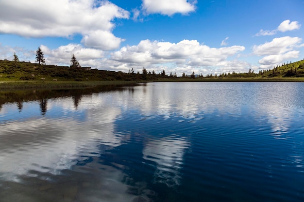 A superfície da água do lago azul é cercada por abetos e montanhas