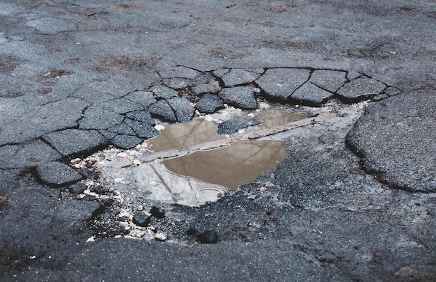 A superfície da estrada pavimentada está danificada poça de asfalto quebrada em estrada rachada