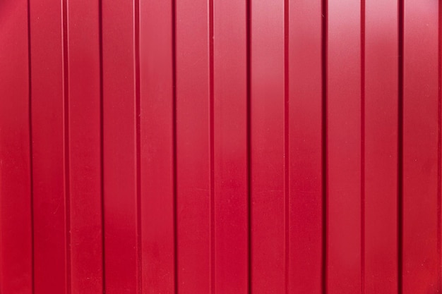 A superfície de uma cerca de ferro vermelho feita de papelão ondulado com listras verticais. Fundo. Espaço para texto.