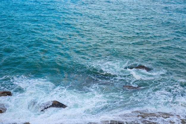 A superfície do mar com a onda e as pedras na vista superior da costa Fundo azul do mar