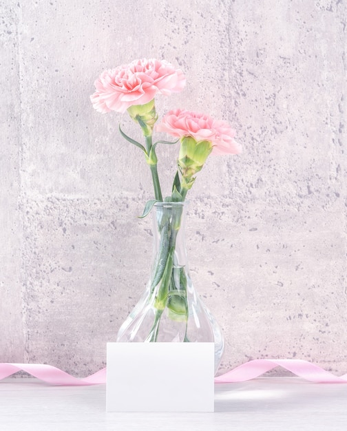 A surpresa da caixa de presente artesanal do dia das mães deseja fotografia - Lindos cravos em flor com uma caixa de fita rosa isolada no design do papel de parede cinza, close-up, copie o espaço, maquete