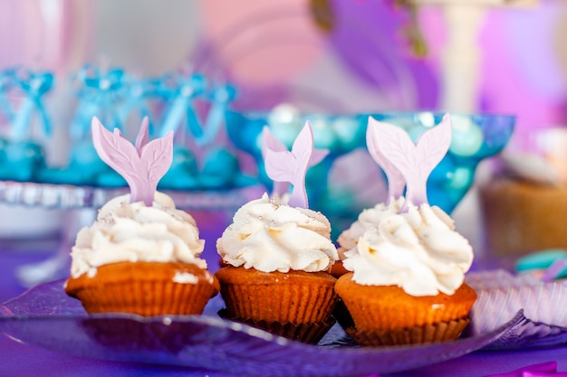 A tabela para miúdos com os cupcakes com cobertura branca decorou a cauda roxa da sereia.