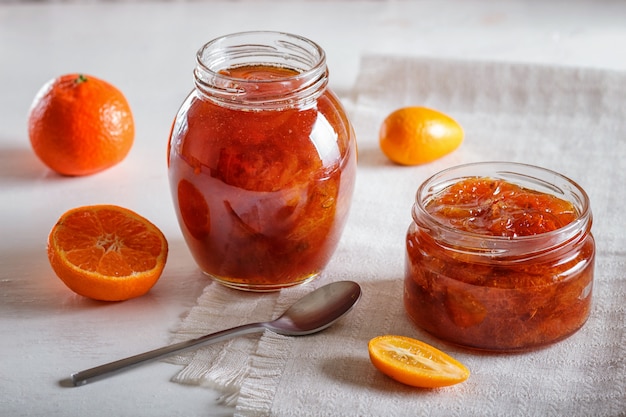 A tangerina e o kumquat bloqueiam em um frasco de vidro na tabela branca.