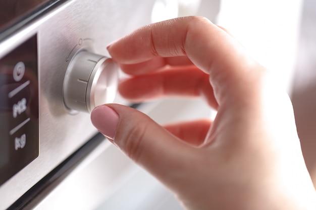 A terra arrendada da mão gira o calor do botão do círculo do seletor do forno micro-ondas para cozinhar o alimento na sala da cozinha em casa, close up.