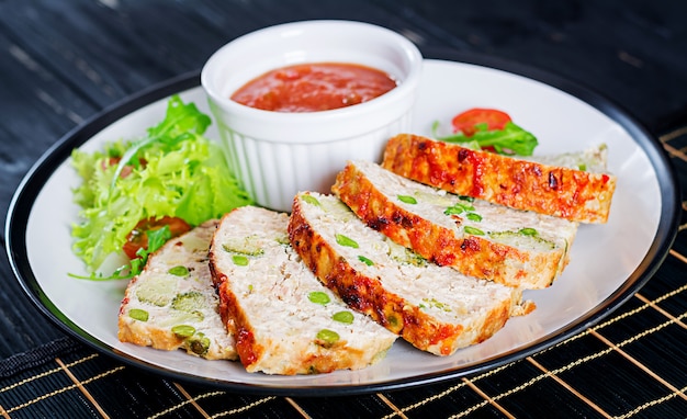 A terra caseiro saboroso cozeu o meatloaf da galinha com ervilhas verdes e brócolis na tabela preta.