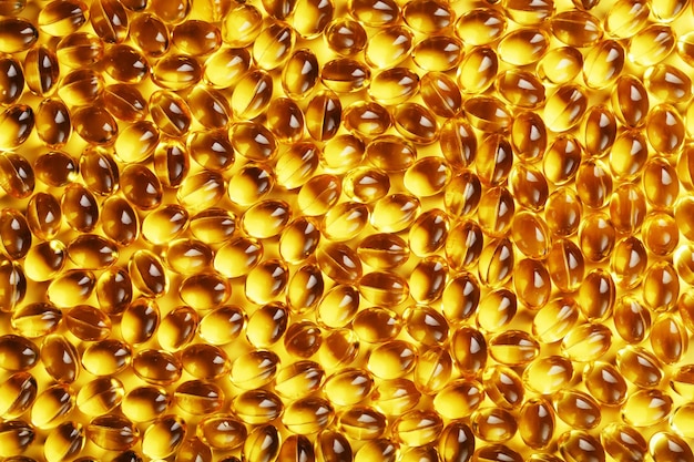 A textura das cápsulas na casca com vitamina D3 líquida em tela cheia Cápsulas de ouro com suplemento alimentar para articulações, dentes e ossos