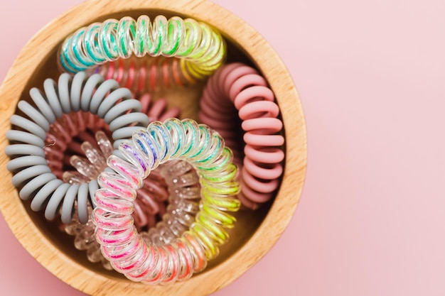 A tigela de madeira de elásticos de cabelo espiral em fundo rosa para o conceito de acessórios femininos