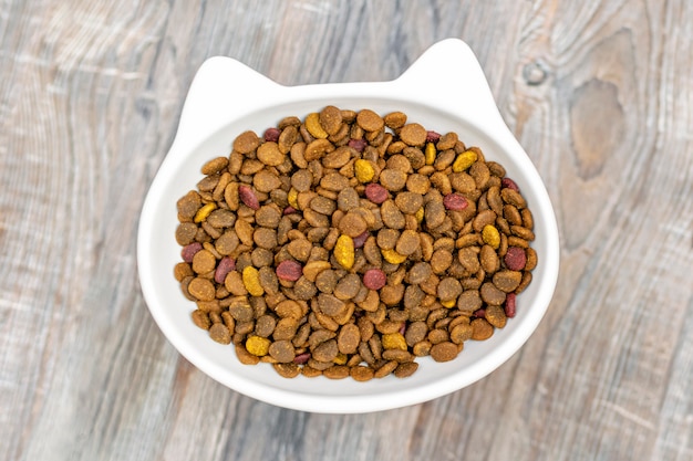 A tigela em forma de cabeça de gato é preenchida com comida seca em cima da mesa de madeira.