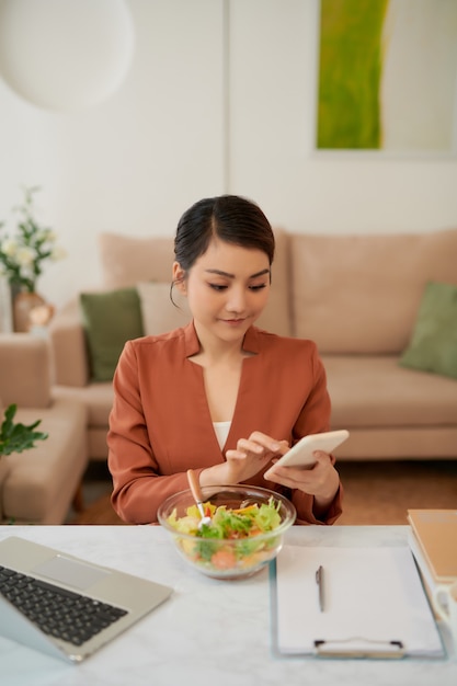 A trabalhar a almoçar em casa mulher atraente com portátil a comer salada