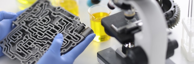 A transmissão automática encontra-se em luvas de borracha na mesa com microscópio e tubos de ensaio em closeup de laboratório químico. controle de qualidade do conceito de óleos de motor.