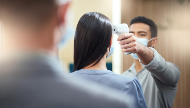 A triagem de Covid é um processo rápido e fácil Foto recortada de uma empresária irreconhecível usando uma máscara e tendo sua temperatura medida enquanto está no início de uma fila em seu escritório