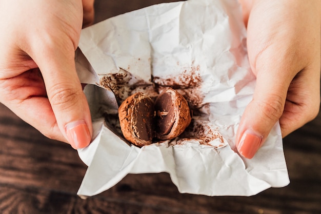 A trufa de chocolate rachada feita com um centro do ganache do chocolate revestido no chocolate, no pó de cacau ou nas porcas brindadas desbastadas dentro do papel envolve essa terra arrendada com mãos.