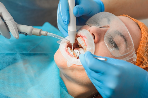 Foto a ultrassonografia do dentista remove pedras nos dentes de uma mulher com uma almofada dentária na boca.