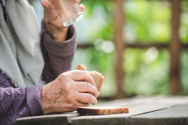 A velha bebe água e come pão em uma velha mesa de madeira em um jardim