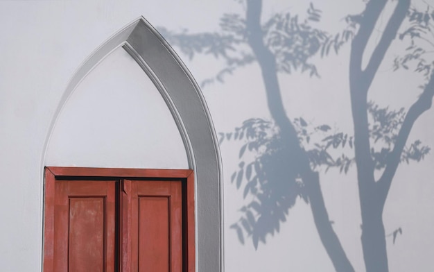 A velha porta de madeira de arco vintage na parede de concreto branco com sombra de árvore na superfície