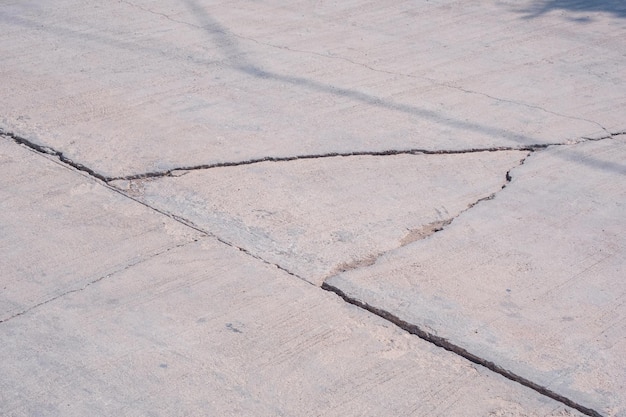 A velha rua de concreto quebrada danificada com colapso e grandes linhas de rachaduras na superfície