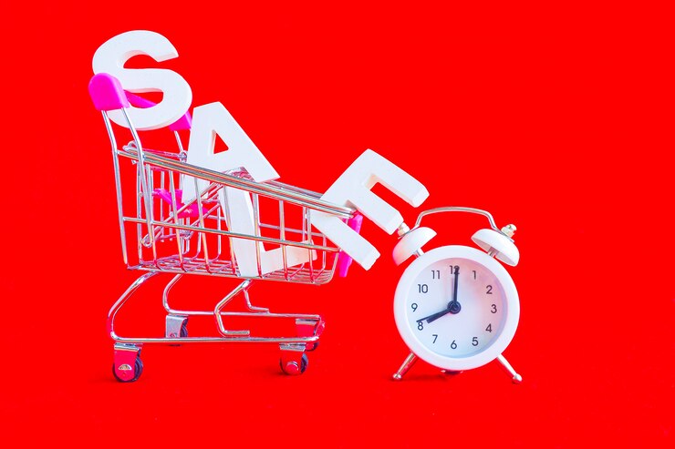 Foto a venda da palavra em letras brancas de volume em um carrinho de compras de metal e um despertador branco ao lado sobre um fundo vermelho.