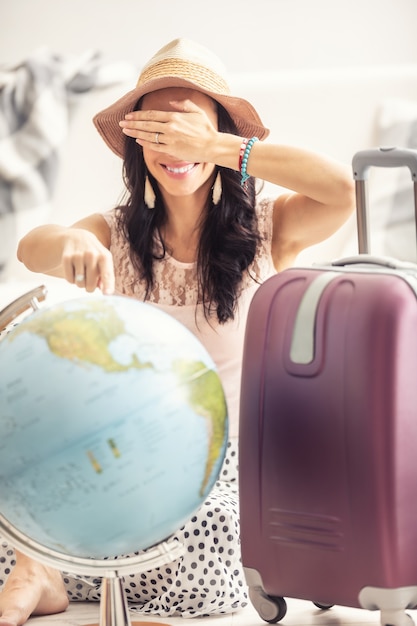 A viajante feminina nas férias de verão está pronta para ir de férias, com a mala pronta, aponte aleatoriamente para o globo com os olhos fechados.