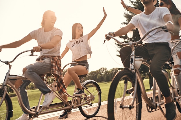 A vida é incrível! Duas jovens mulheres modernas dando high five enquanto pedalavam com amigos ao ar livre