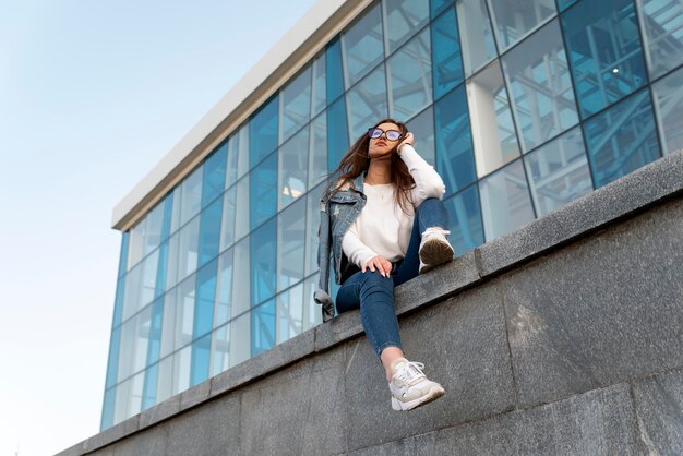 A visão inferior da jovem estudante está descansando na rua da cidade Jovem elegante em roupas da moda jovem