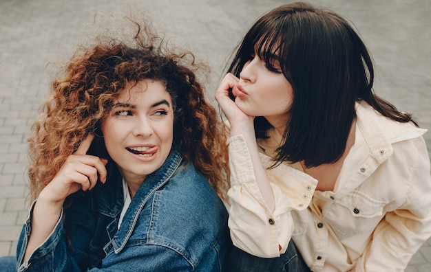A visão superior de duas garotas expressivas com cabelos cacheados que posam do lado de fora e se divertindo juntas