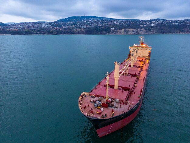 A vista aérea de um graneleiro à noite mostra uma exibição impressionante de luzes refletidas na água enquanto o enorme navio corta as ondas