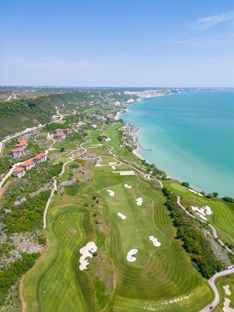 A vista aérea do campo de golfe estende-se sob os seus fairways verdejantes, complementando o deslumbrante panorama costeiro