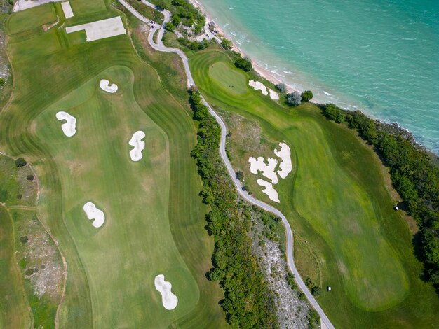 A vista aérea do campo de golfe estende-se sob os seus fairways verdejantes, complementando o deslumbrante panorama costeiro