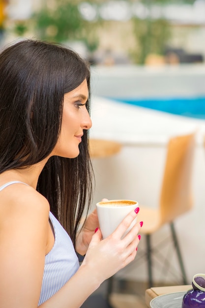 A vista lateral de uma jovem tomando café e descansando no resort em um café ao ar livre