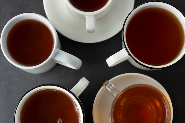 A vista superior de muitos copos, canecas com chá quente bebe na obscuridade, copyspace. Hora do chá ou freio de chá. Bebida de outono. Imagem enfraquecida com xícaras de chá.