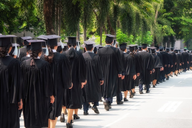 A vista traseira do grupo de graduados da universidade em vestidos pretos alinha-se para o diploma na cerimônia de graduação da universidade.