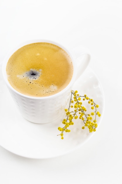 A xícara de café branca em uma tabela branca com mimosa amarela floresce. Minimalismo.