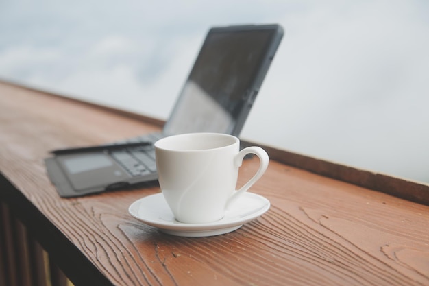 A xícara de café do teclado do monitor do computador e o mouse com espaço em branco estão na mesa de trabalho no rio da montanha do céu e no fundo da vista frontal das árvores