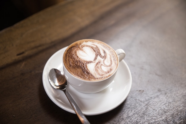 A xícara de cappucino quente está na mesa de madeira. É uma arte no café com leite.