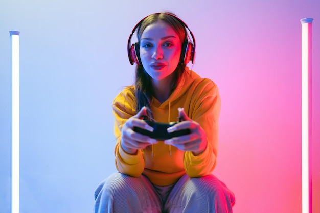 a young woman in a yellow hoodie and headphones plays video games surrounded by colorful lights