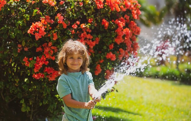 Aadorable Kid Boy Bewässerung der Pflanzen aus Schlauchspray mit Wasserschlauch im Garten im Hinterhof