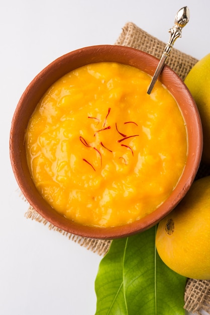 Foto aam ras ist ein köstliches indisches saisonales dessertrezept, aamras ist einfaches haapus- oder alphonso-mango-püree oder pulp mit safran, kesar-topping. serviert in einer terrakottaschüssel auf buntem hintergrund.