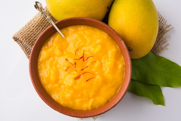 Aam Ras ist ein köstliches indisches saisonales Dessertrezept, Aamras ist einfaches Haapus- oder Alphonso-Mango-Püree oder Pulp mit Safran, Kesar-Topping. Serviert in einer Terrakottaschüssel auf buntem Hintergrund.