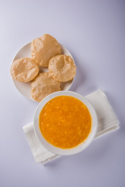 Aam Ras Puri ist ein köstliches indisches Rezept, das als saisonales Dessert serviert wird, Aamras ist einfaches Mango-Püree oder Fruchtfleisch, serviert in einer Keramikschale und einem Teller auf buntem oder hölzernem Hintergrund. Selektiver Fokus