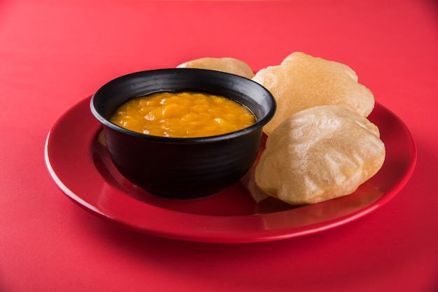 Aam Ras Puri ist ein köstliches indisches Rezept, das als saisonales Dessert serviert wird, Aamras ist einfaches Mango-Püree oder Fruchtfleisch, serviert in einer Keramikschale und einem Teller auf buntem oder hölzernem Hintergrund. Selektiver Fokus