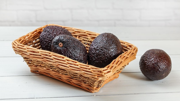 Abacates marrons escuros (cultivar Bilse) em cesta quadrada na mesa de quadros brancos.