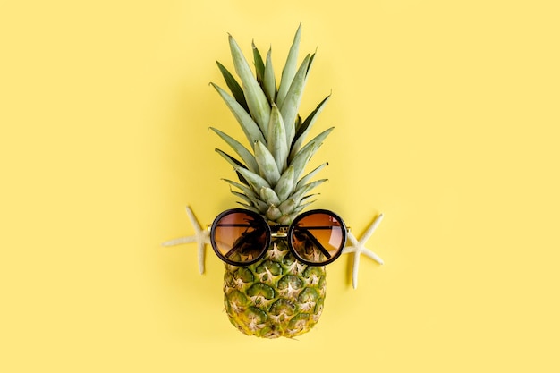 Abacaxi hipster em óculos de sol em fundo amarelo fundo de verão plano lay