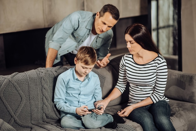 Abaixe isso. Pais jovens e simpáticos tentando convencer o filho pré-adolescente a parar de brincar no telefone dele enquanto o menino fica relutante