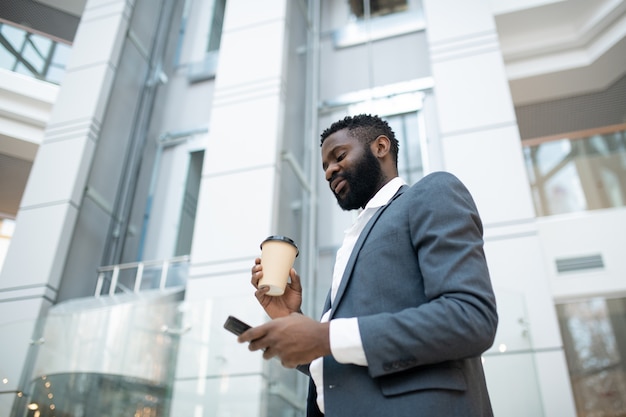 Abaixo, a imagem do empresário negro barbudo com uma jaqueta respondendo no Messenger e bebendo café em movimento