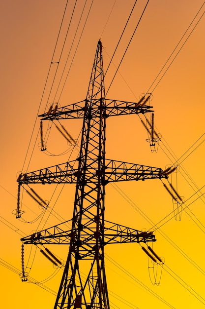 Abaixo vista de ângulo de postes de eletricidade que transportam eletricidade para uma cidade ou cidade Fundo laranja do pôr do sol