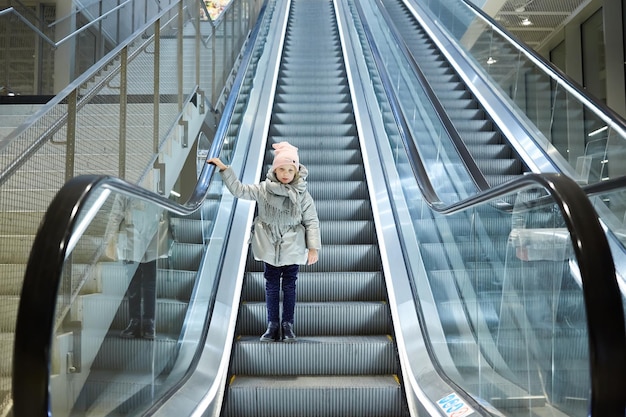 Desde abajo, una foto de una chica parada en una escalera móvil en la terminal