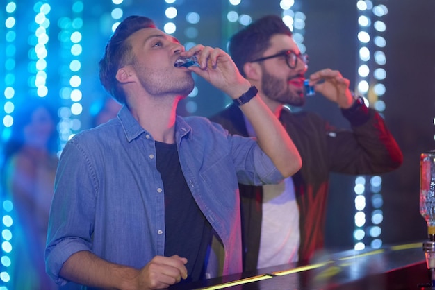 Foto abajo en una toma de dos tipos bebiendo trago en la barra del bar en un club nocturno